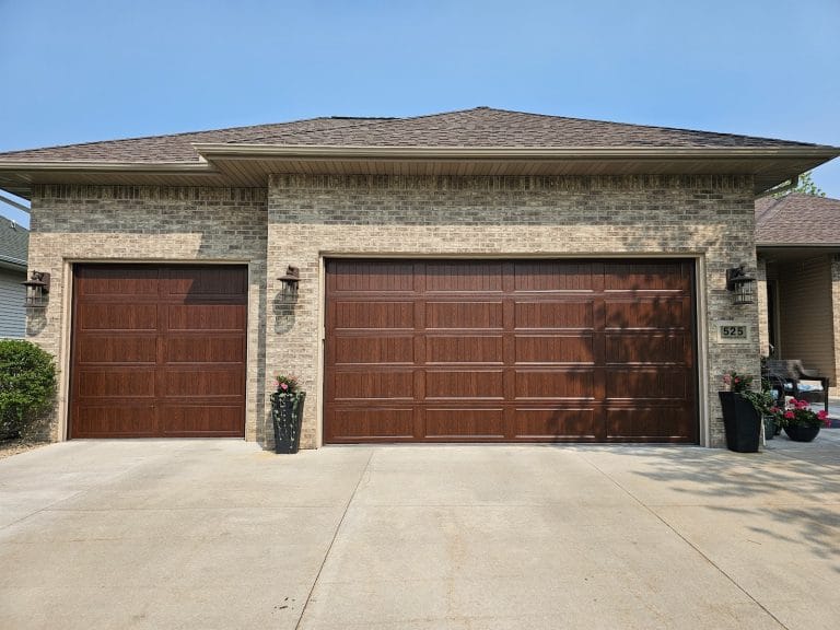 Brown carriage-style steel garage doors on a stone and brick home, finished job by David's Urgent Garage Door, Twin Cities MN