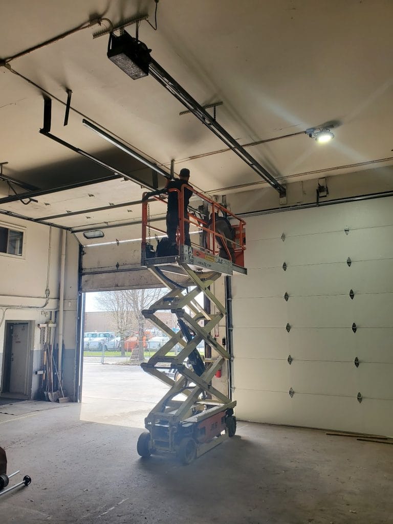 David repairing a tall commercial sectional door from a scissor lift in a Minnesota warehouse