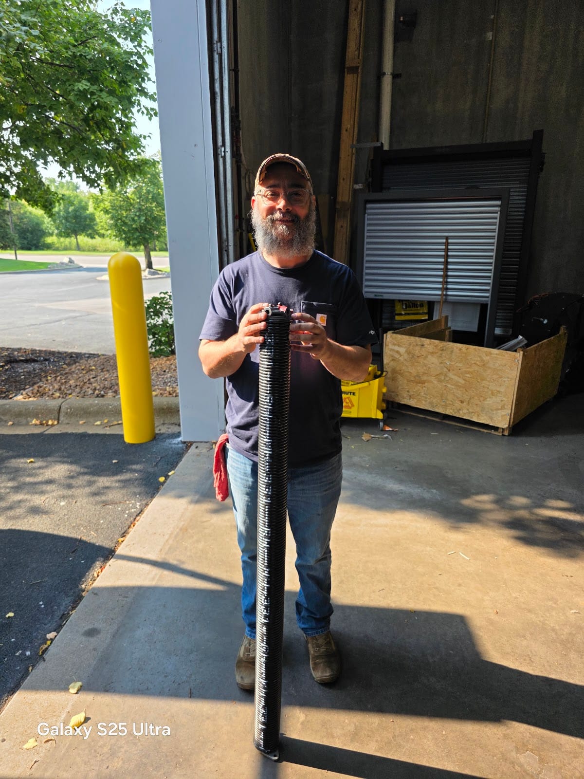David holding a new torsion spring outside a commercial garage door