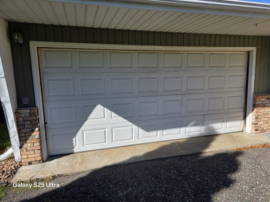 Older white short raised-panel steel garage door with a dented bottom section, the kind of door we replace, Twin Cities MN