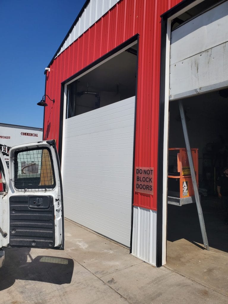 New white commercial sectional door installed on a red steel building in Minnesota