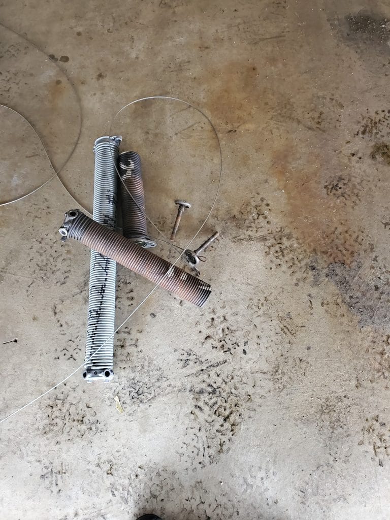 Rusted garage door extension spring and tangled lift cable removed during repair