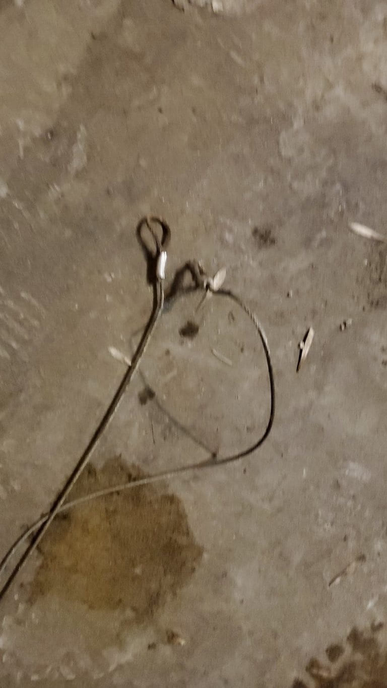 Snapped garage door lift cable with frayed, rusted end on a Minnesota garage floor
