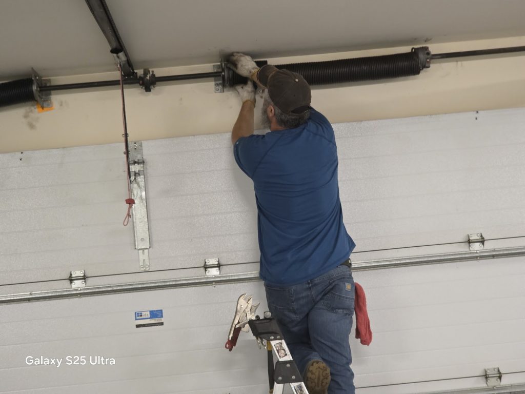David installing a new torsion spring above a white insulated garage door