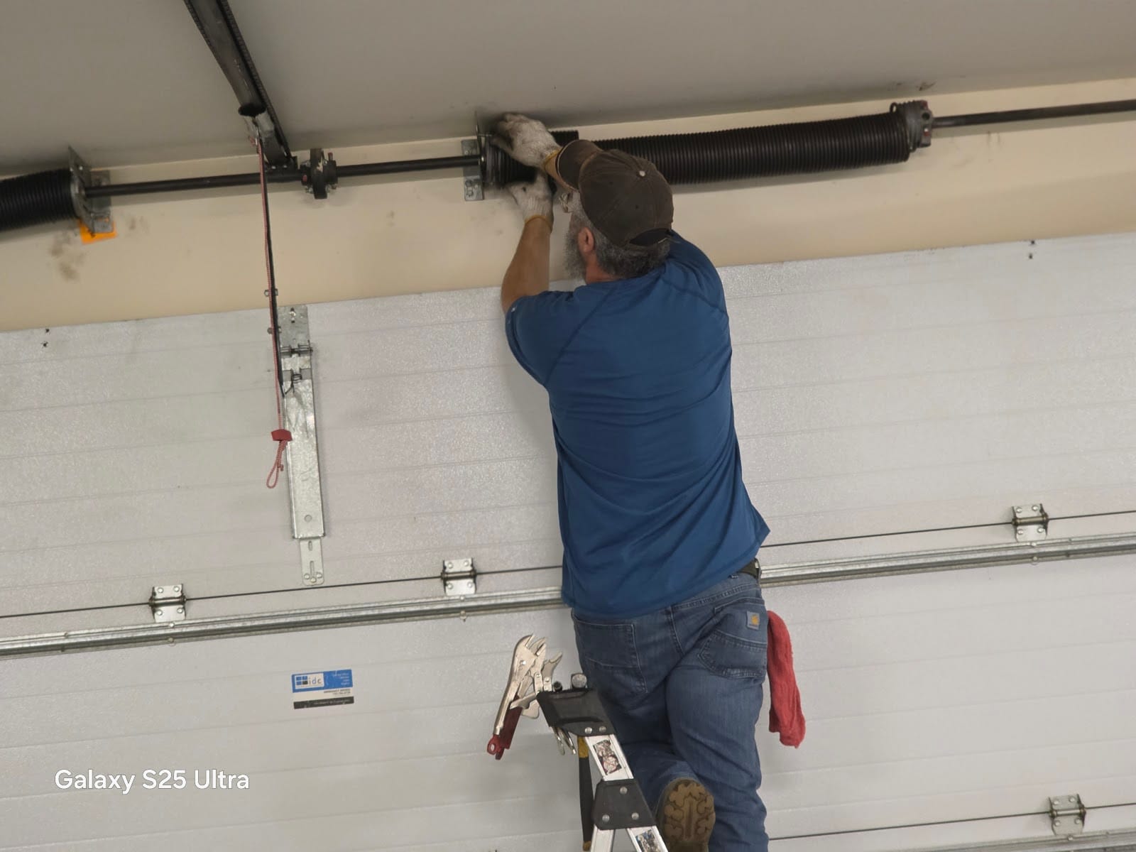 David on a ladder installing the torsion spring assembly above a new white garage door, Minnesota