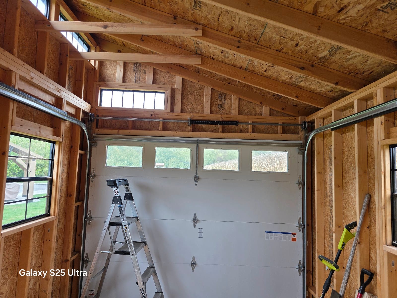 Newly installed white garage door with a row of windows, inside a wood-framed garage
