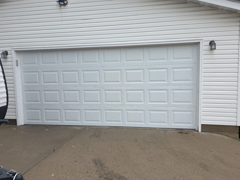 New white raised-panel double garage door installed on a house with white siding