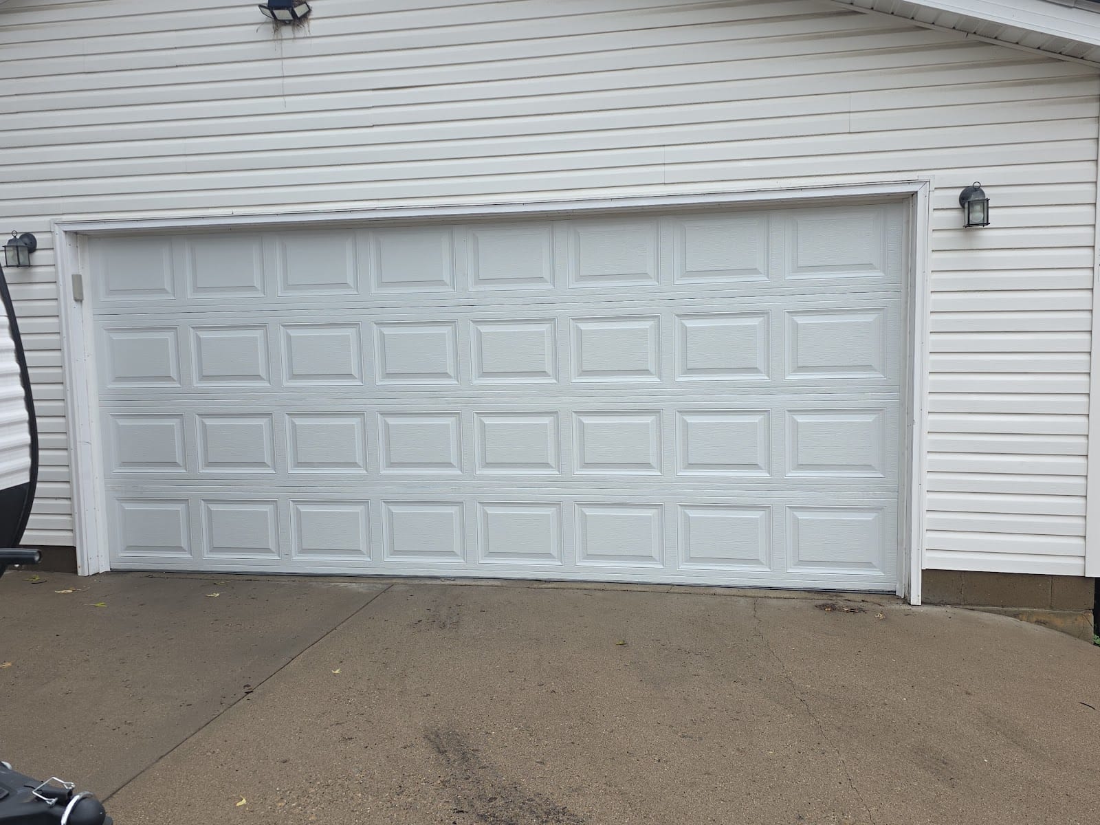 New white raised-panel double garage door installed on a house with white siding